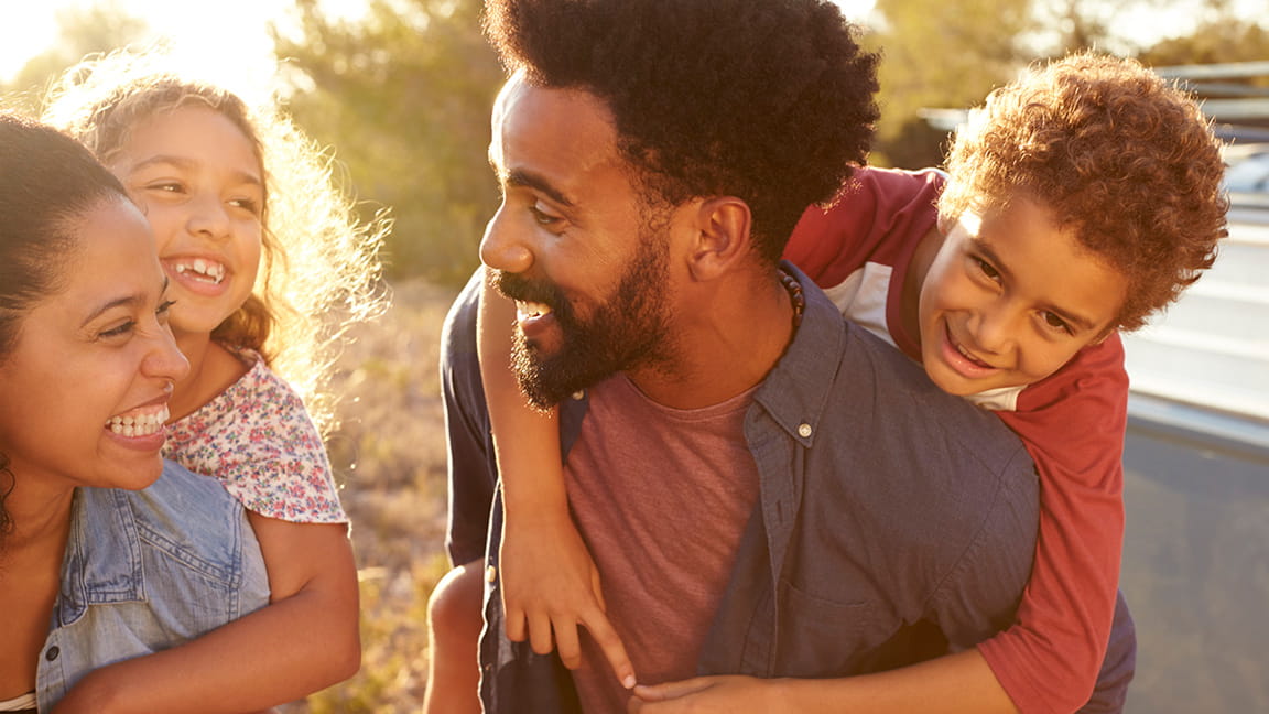 happy parents giving kids piggyback ride outdoors