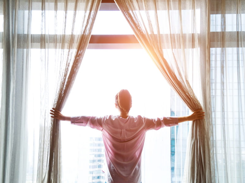 woman opens curtains to sunrise