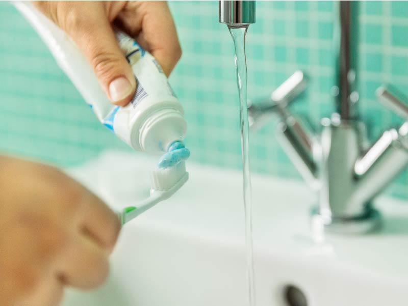 Hands holding toothbrush and paste at sink.