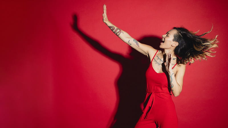 Young tattooed woman in a red jumpsuit dancing in front of a red background Young tattooed woman in a red jumpsuit dancing in front of a red background