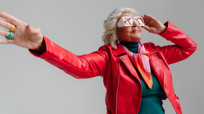 Cool older woman in a red leather jacket and trendy eyeglasses dancing on a grey background Cool older woman in a red leather jacket and trendy eyeglasses dancing on a grey background