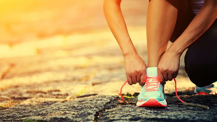 Woman tying workout sneaker outdoors at sunrise or sunset