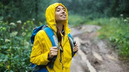 Young woman in raincoat enjoys nature in the rain