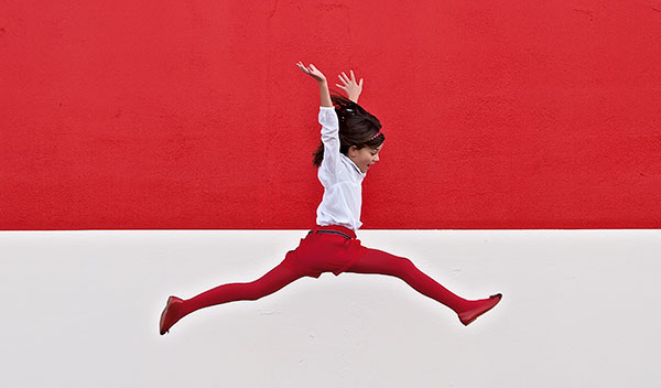 Girl jumping in front of red background Getty_137885806 Girl jumping in front of red background