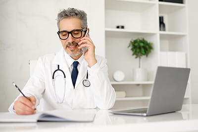a doctor in his office at his desk, talking on the phone