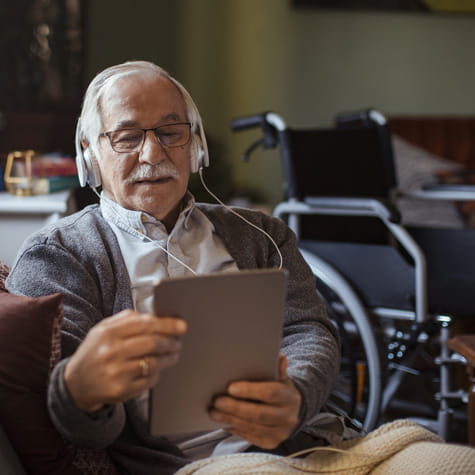 Stroke patient sitting on couch holding iPad and headphones.