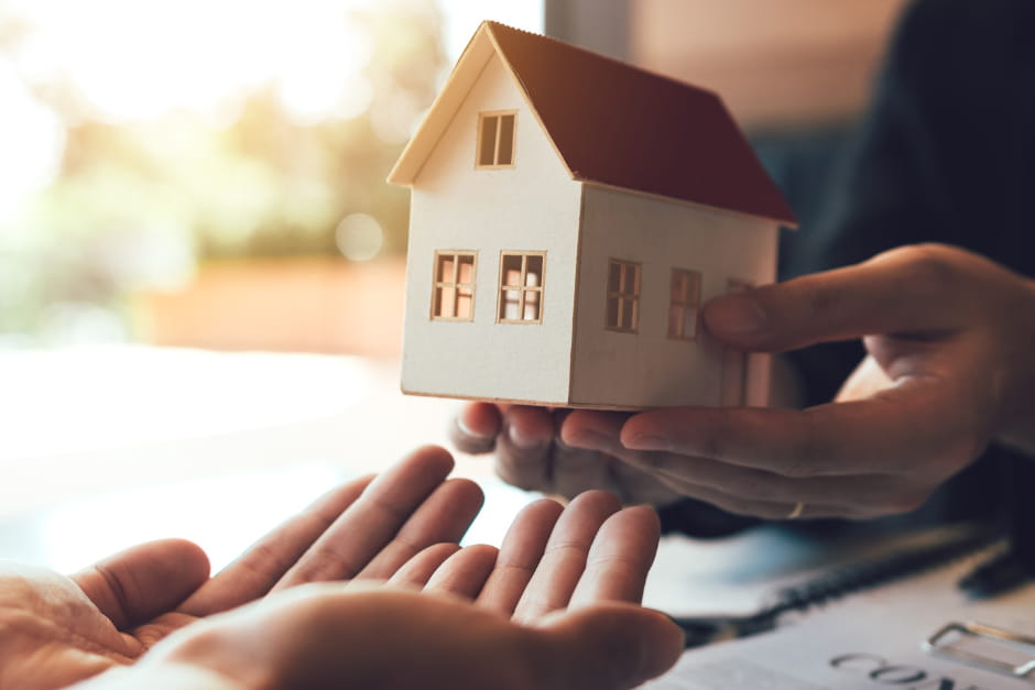 hands holding out a small model house to another pair of hands